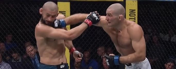 Two muscular bald MMA fighters exchange punches inside a fenced octagon during a match.