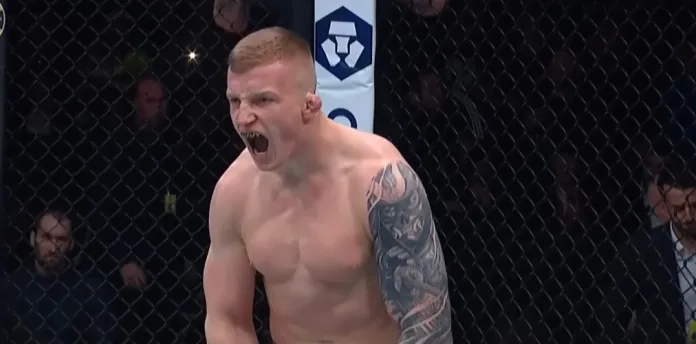 Shirtless MMA fighter with a full left-arm sleeve tattoo screaming inside the cage during a match.