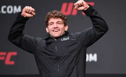 Man in a black USA jacket smiles and raises both fists in celebration on stage.