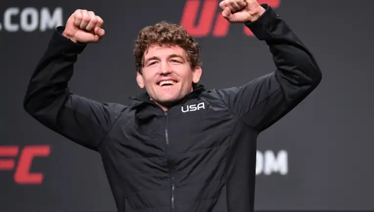 Man in a black USA jacket smiles and raises both fists in celebration on stage.