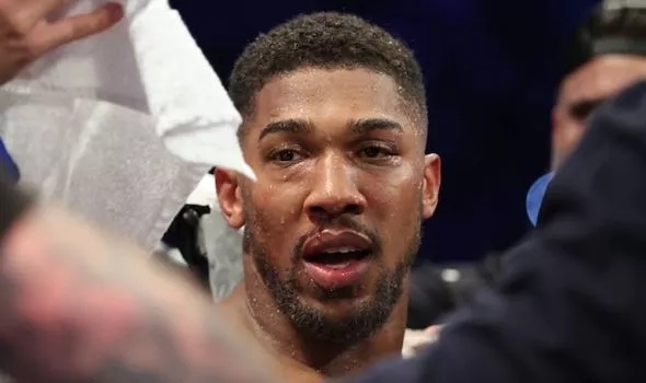 Close-up of a male athlete in a boxing ring, face sweaty and focused, with towels and people in the background.