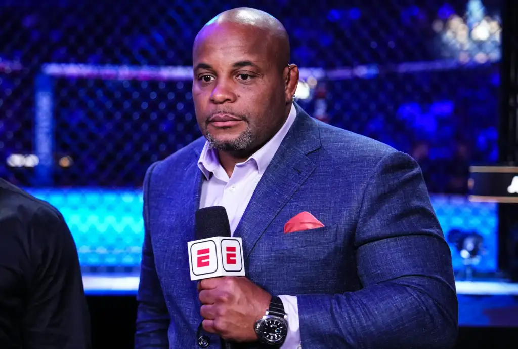 2185167126 2 - AfroCombat Man in a blue blazer being interviewed at a sports event, holding an ESPN microphone with a pink pocket square visible; blue arena lighting in background.