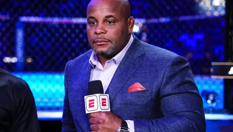 Man in a blue blazer being interviewed at a sports event, holding an ESPN microphone with a pink pocket square visible; blue arena lighting in background.