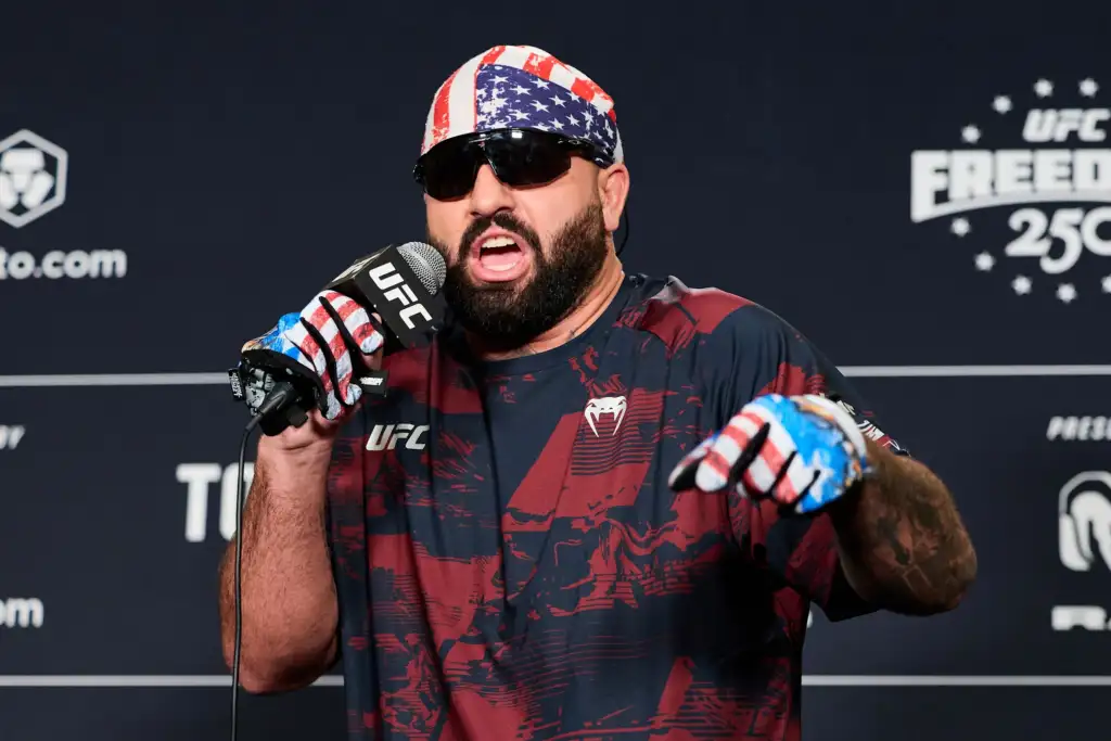 4066daa2284502f53ff573b2ec0c41f7 - AfroCombat MMA fighter wearing a red, white, and blue bandana speaks into a UFC microphone at a press event, with sunglasses and a beard.