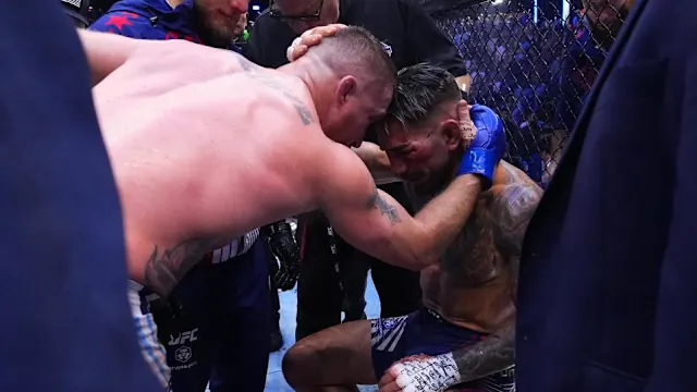 Intense moment in a cage fight: two MMA fighters grapple as teammates lean in nearby.