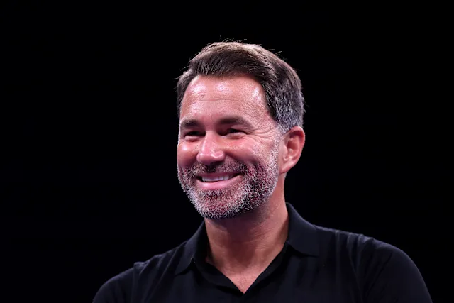 Smiling man with a salt-and-pepper beard wearing a black polo shirt against a dark background.