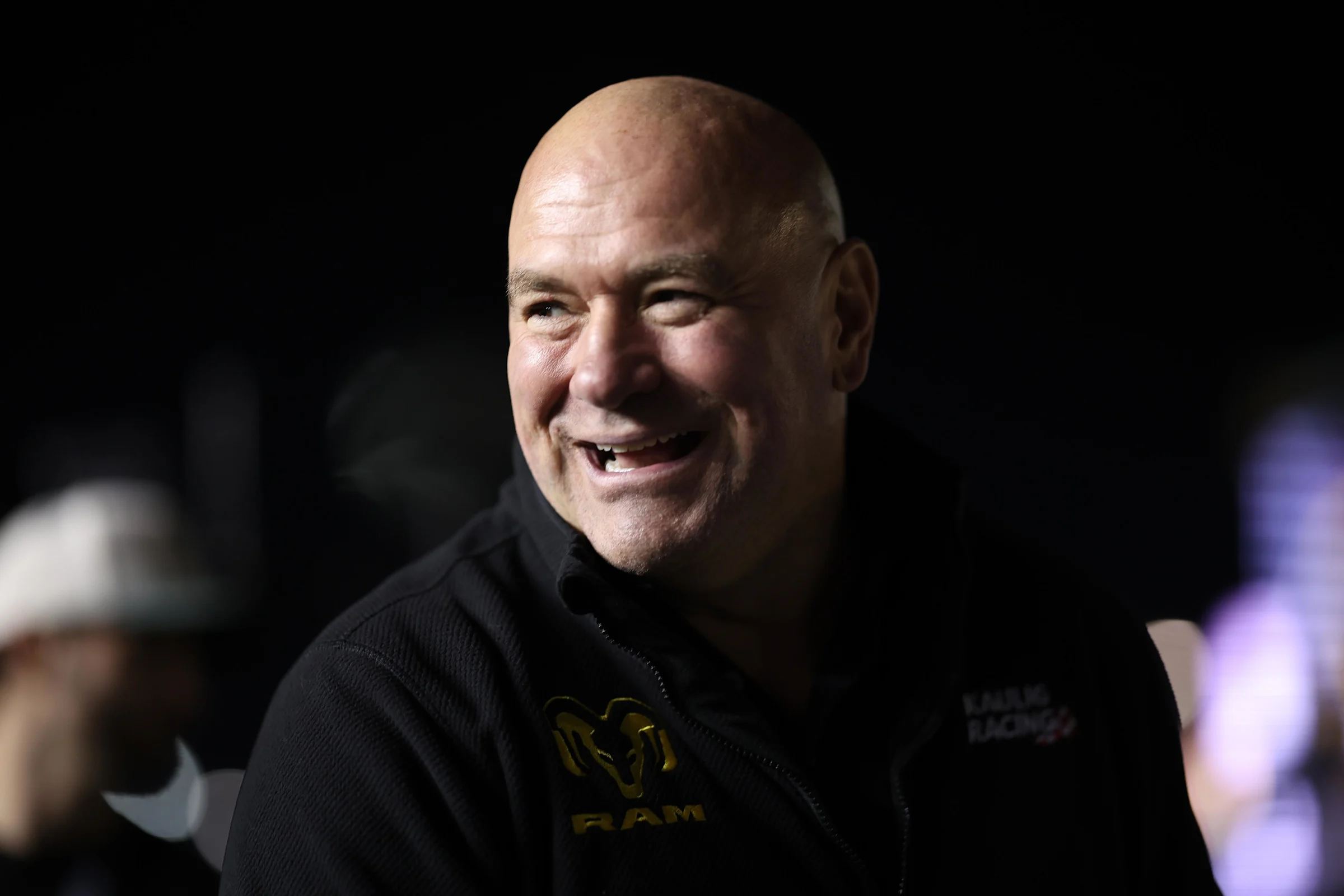 82beedd57f22db9003db13c841263be0 - AfroCombat Smiling, bald man in a dark setting, wearing a black zip-up jacket.