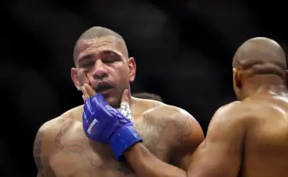 Boxer with a bleeding cheek in a fight, wearing blue gloves, touching his own face while another opponent stands nearby.
