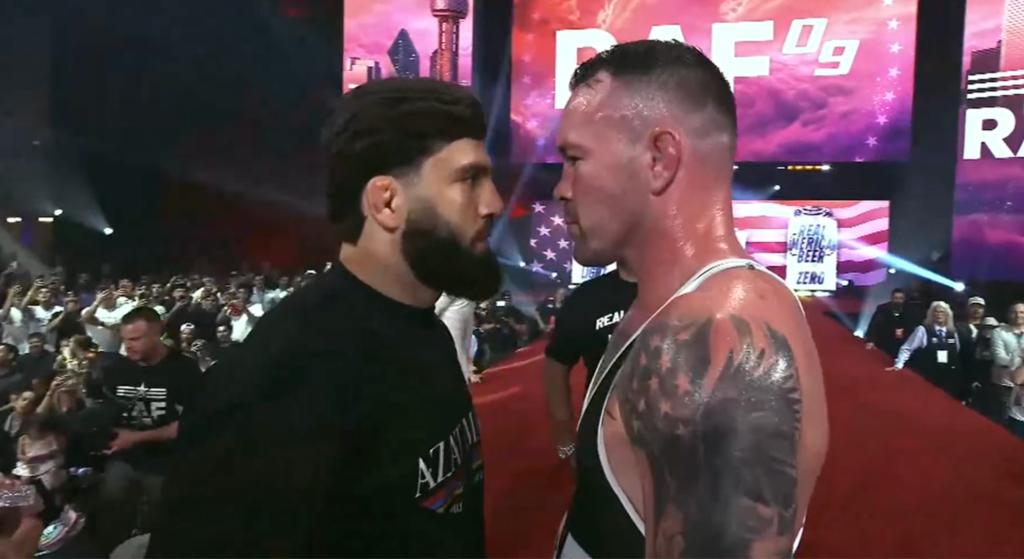 Two male fighters nose-to-nose before a match in a packed arena, with a purple stage backdrop and spectators watching.