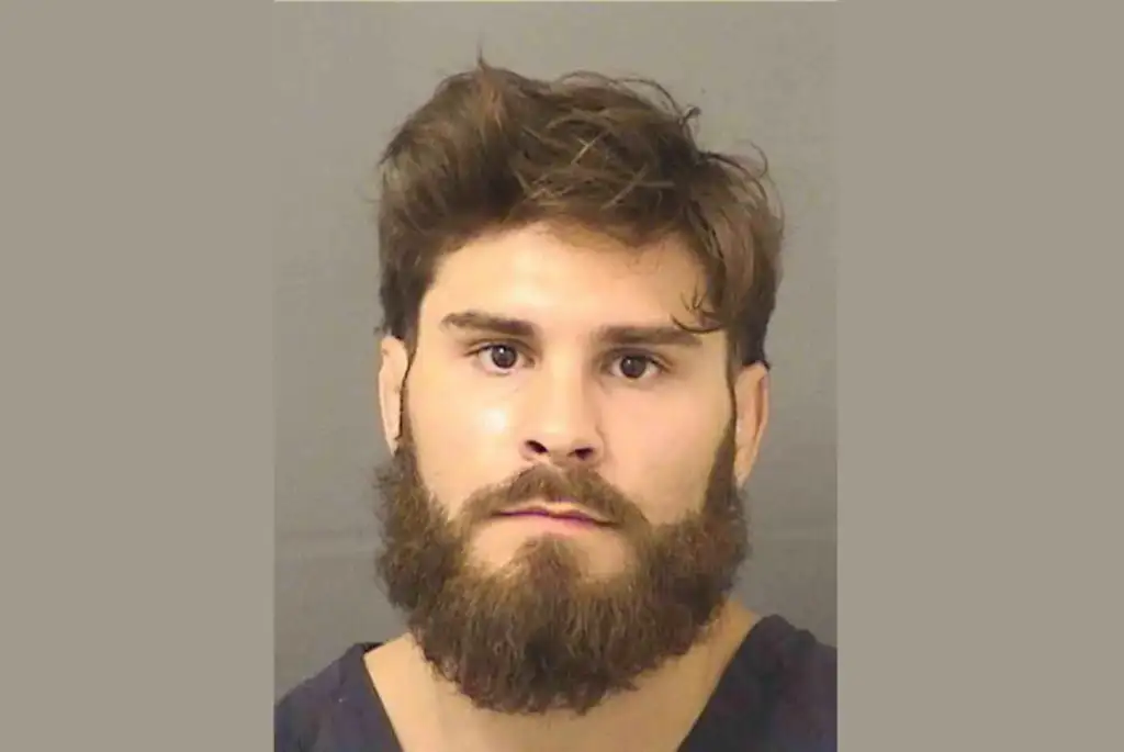 Booking photo of a man with brown hair and full beard against a gray backdrop.