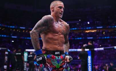 UFC fighter with tattoos and colorful floral shorts standing in the octagon, shirtless and looking intense as the crowd watches.