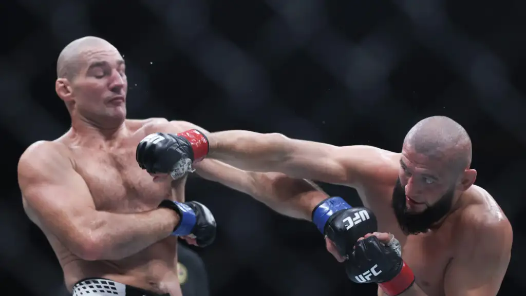 Two muscular UFC fighters in a cage exchange punches, one landing a punch to the other's head.