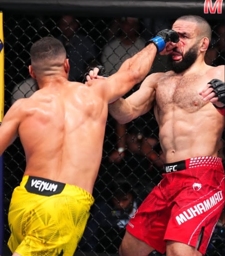 Oplus_131072 - AfroCombat Two shirtless mixed martial artists punch at each other inside a cage, one wearing yellow Venum shorts and the other red Muhammad shorts.