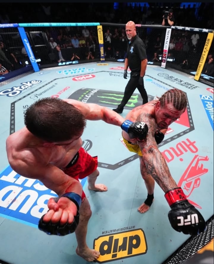 Two mixed martial artists exchange strikes inside the UFC octagon as a referee watches from behind the cage.