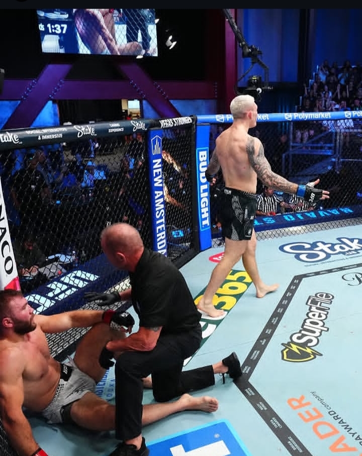 MMA referee tends to a fallen fighter inside the cage while a standing fighter watches nearby.