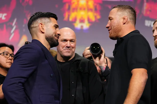 Two fighters face off in a stare-down on stage before a UFC event, with photographers and crew watching in the background.