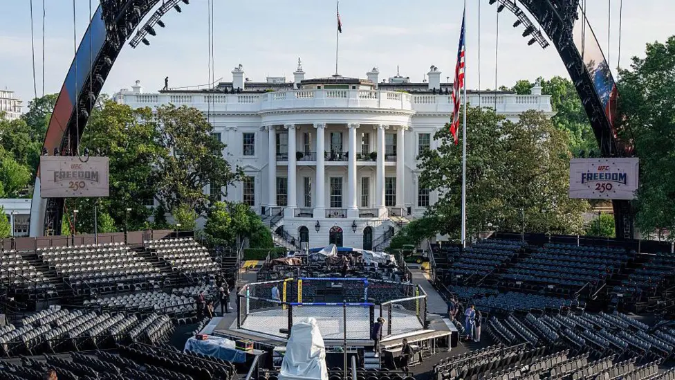 c5237880-66a1-11f1-80bb-fb4d08542828jpg - AfroCombat UFC octagon setup in front of the White House with empty stadium seating surrounding a fenced MMA cage.