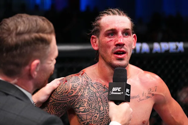 UFC fighter with tribal tattoos being interviewed in the cage, microphone held to his mouth.