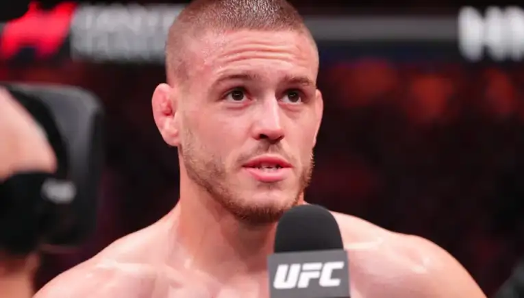 Male UFC fighter answering questions during a post-fight interview, holding a UFC-branded microphone in the octagon.