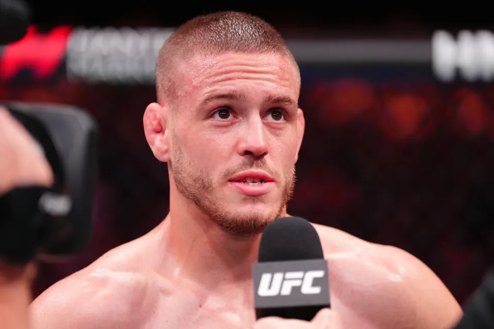 Male UFC fighter answering questions during a post-fight interview, holding a UFC-branded microphone in the octagon.
