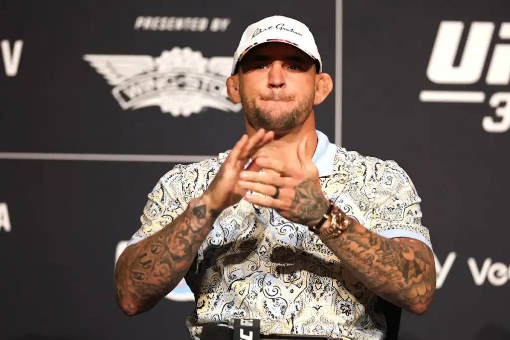de07aab1-9c39-4b2c-9b6b-6f8491f8c17b - AfroCombat Tattooed male fighter wearing a white cap and a patterned polo speaks at a press conference, hands together in front.