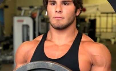 Young muscular man in a black tank top holding a weight plate in a gym.