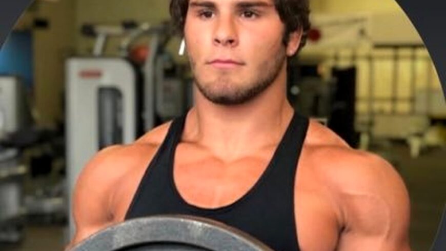 Young muscular man in a black tank top holding a weight plate in a gym.