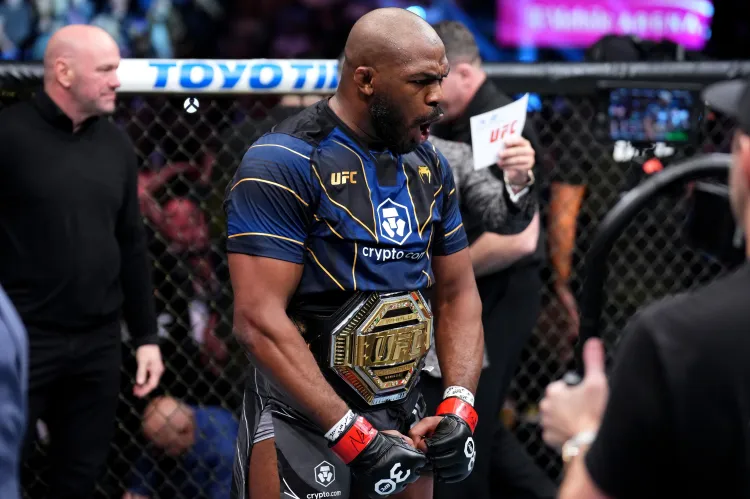 UFC fighter in blue kit with a gold championship belt around his waist inside the octagon, fists clenched in celebration.