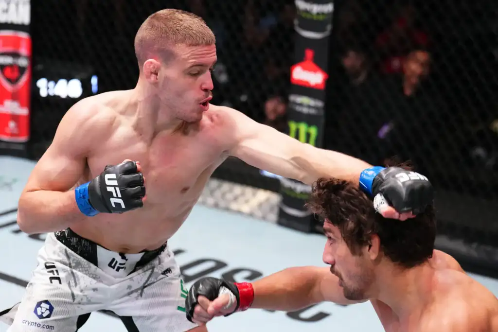 Two shirtless mixed martial artists in a UFC cage exchanging punches mid-fight; one lands a punch while the other braces