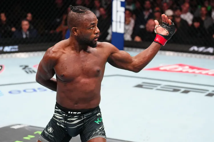 gettyimages-2190008681 - AfroCombat Male mixed martial artist inside the UFC cage raises his right arm in victory after a match, wearing black fight shorts and red wrist wraps.