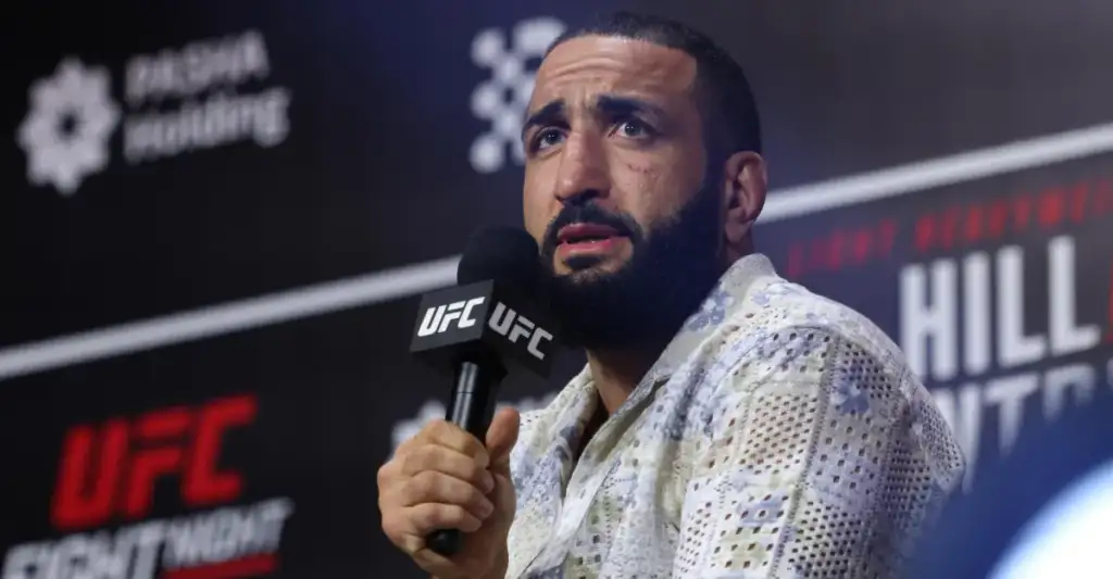 Man with a beard speaks into a UFC-branded microphone at a press conference.