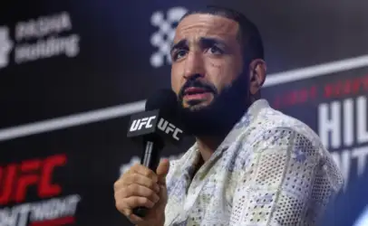 Man with a beard speaks into a UFC-branded microphone at a press conference.