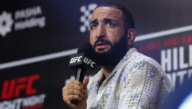 Man with a beard speaks into a UFC-branded microphone at a press conference.
