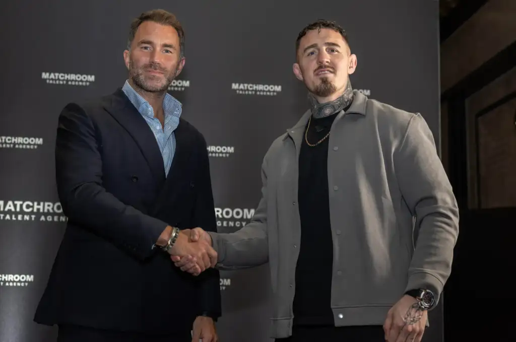 Two men in smart casual attire shake hands in front of a dark backdrop with 'MATCHROOM TALENT AGENCY' logos visible.