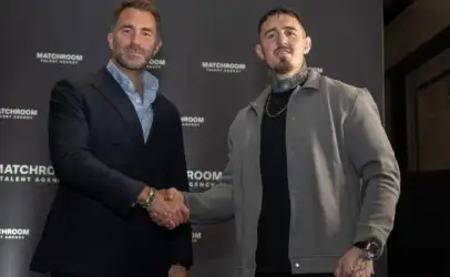 Two men in smart casual attire shake hands in front of a dark backdrop with 'MATCHROOM TALENT AGENCY' logos visible.