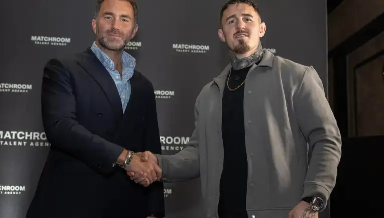 Two men in smart casual attire shake hands in front of a dark backdrop with 'MATCHROOM TALENT AGENCY' logos visible.