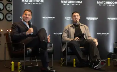 Two men sit on stage in chairs during a panel, each holding a microphone; backdrop says Matchroom Talent Agency.