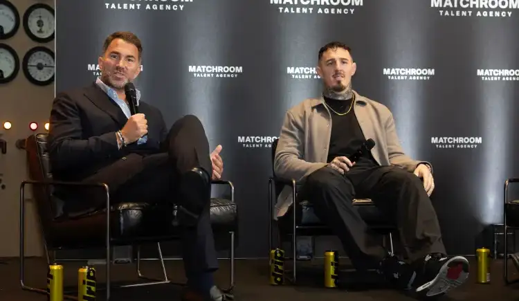Two men sit on stage in chairs during a panel, each holding a microphone; backdrop says Matchroom Talent Agency.