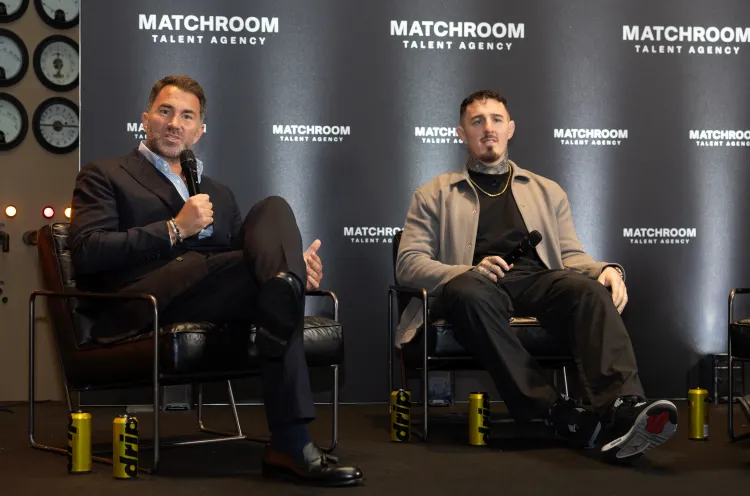 Two men sit on stage in chairs during a panel, each holding a microphone; backdrop says Matchroom Talent Agency.