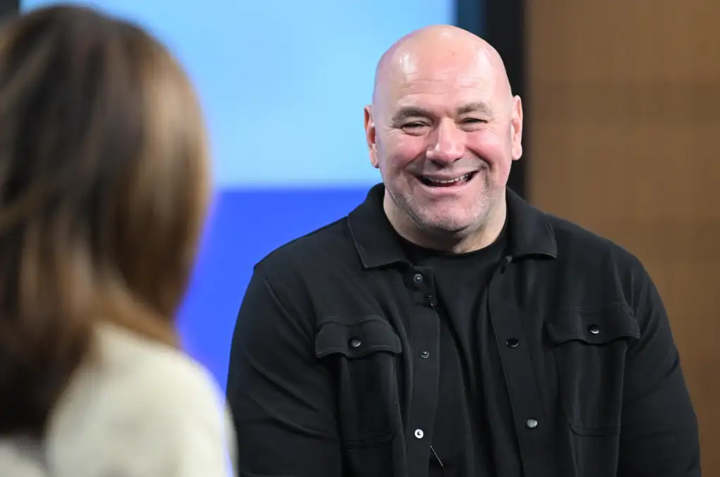 Smiling bald man in a black shirt talks to someone off-camera at an indoor event.