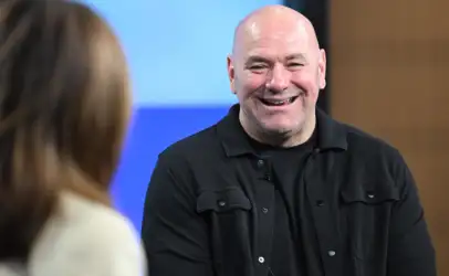 Smiling bald man in a black shirt talks to someone off-camera at an indoor event.