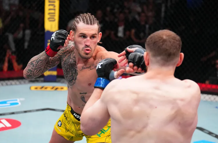 MMA fighter with braided hair and tattoos throws a punch toward his opponent in the cage, wearing yellow trunks and black gloves.