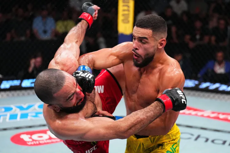 gettyimages-2280251629 - AfroCombat Two male mixed martial artists grapple inside the octagon; one in red shorts lands a punch while the other wears yellow shorts and blocks with his arms.
