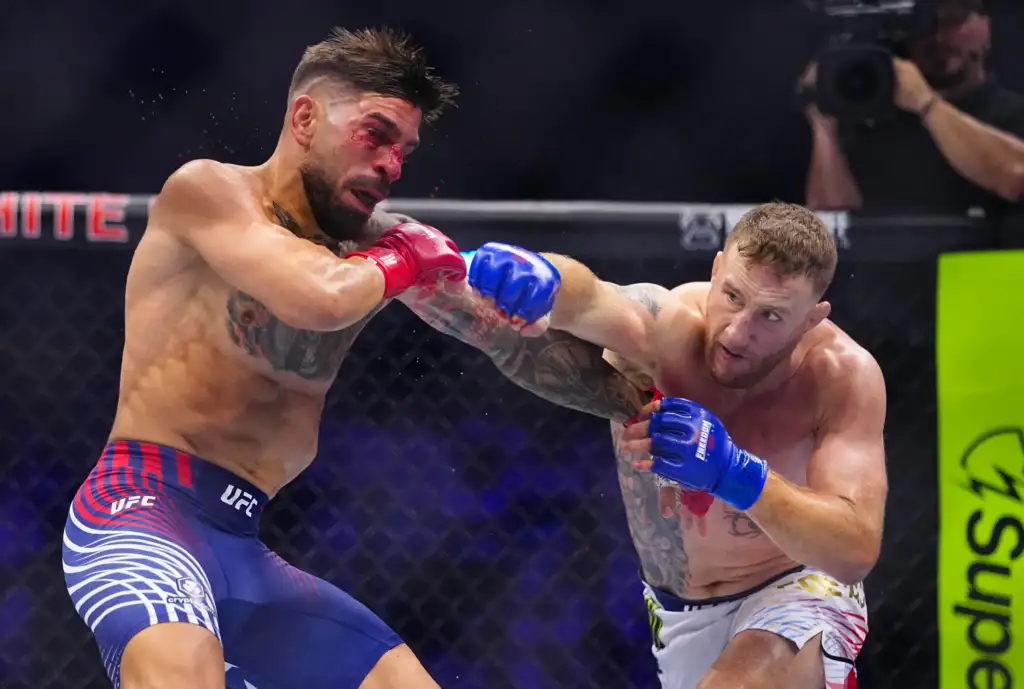 Two shirtless mixed martial artists clash in a UFC fight inside the octagon; one lands a punch while the other blocks with blue gloves.