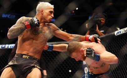 Two UFC fighters clash inside the octagon: one lands a punch on the other's head while the other blocks with his guard up, both shirtless and tattooed.