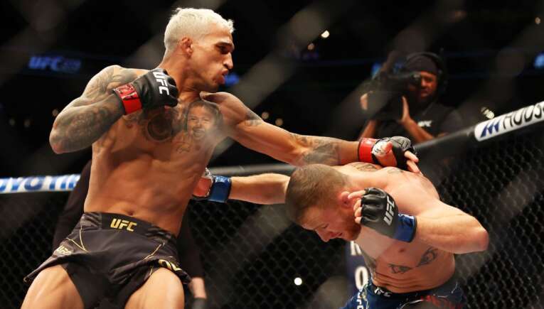 Two UFC fighters clash inside the octagon: one lands a punch on the other's head while the other blocks with his guard up, both shirtless and tattooed.