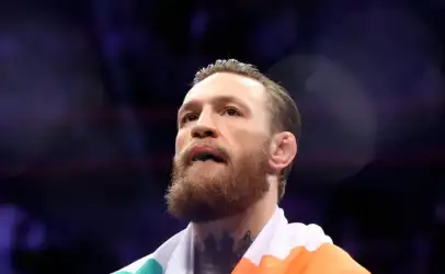 Close-up of a bearded man in a boxing ring, wrapped in an Irish flag, looking up with a focused expression.