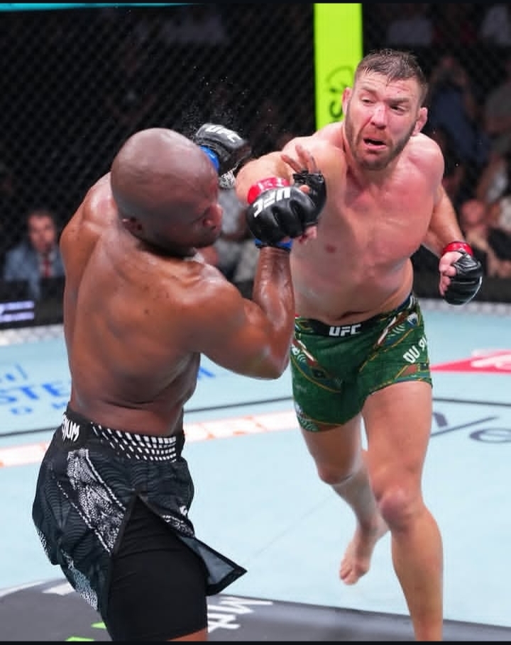 Oplus_131072 - AfroCombat Two UFC fighters clash in the octagon as a punch connects between a black man in black shorts and a lighter man in green shorts with red gloves, inside the cage.