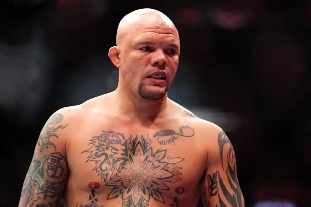 Bald, tattooed male fighter in an arena looking to the side, shirtless in the ring