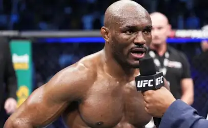 Professional UFC fighter, shirtless and sweaty, speaking into a UFC-branded microphone during a post-fight interview inside the octagon.